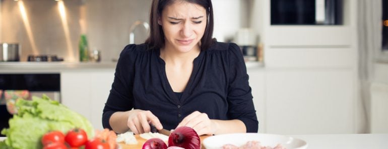 Young housewife cutting onion & crying