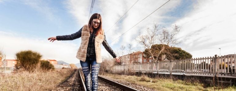 Beautiful Young Woman Walking in Balance on Railway Tracks. The Railroad is in a Residential Area. The Girl has a Casual Look.