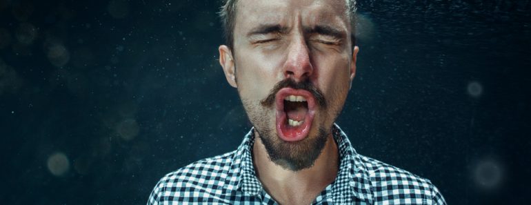 Young funny handsome man with beard and mustache sneezing with spray and small drops, studio portrait on black background(Master1305)s