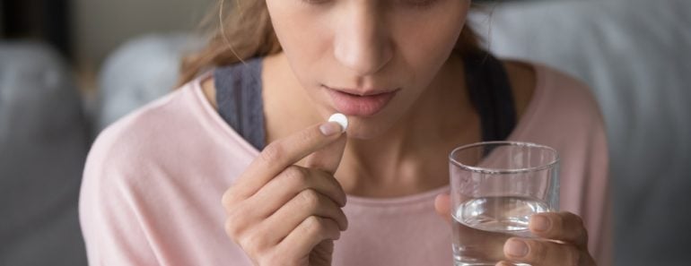 Serious stressed sick millennial mixed race woman holding and thinking over taking round white pill and glass of water(fizkes)s